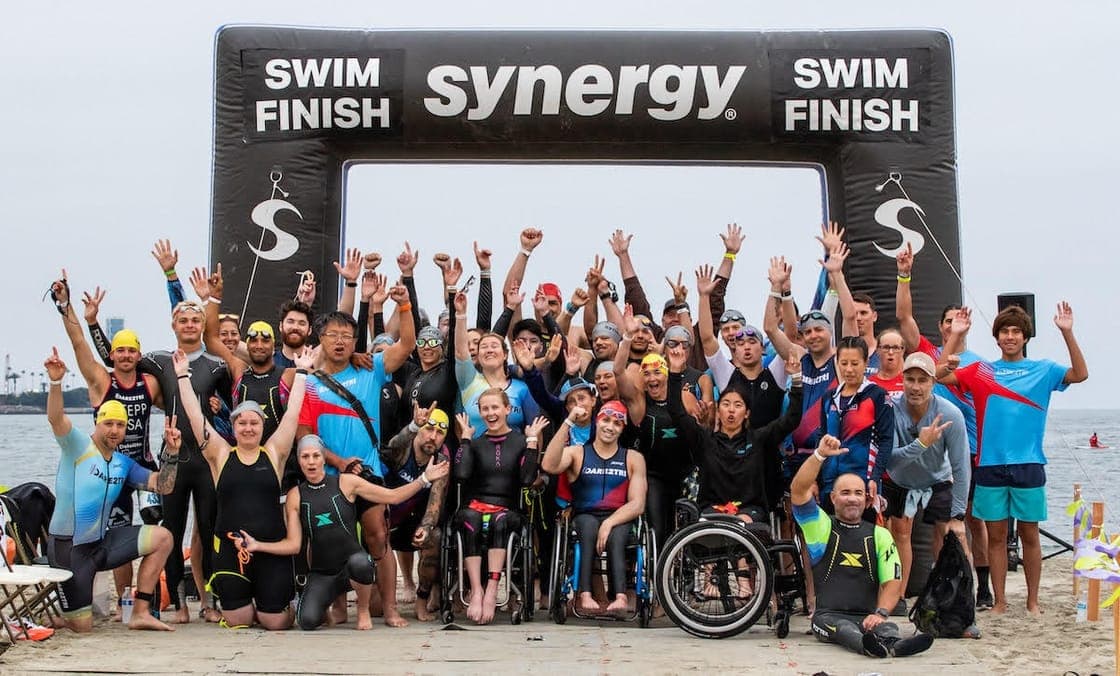 Dare2Tri athletes and supporters celebrating together under a swim-finish arch