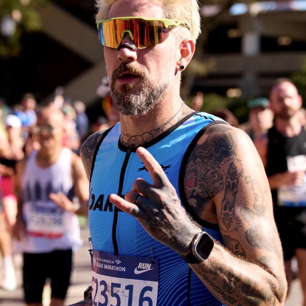 Mid-race at the 2025 Chicago Marathon, sunglasses on, hand up for the camera